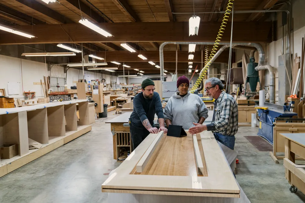 Three makers around a workbench, reviewing drawings together.