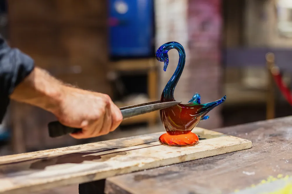 A glassblower turning a gather of molten glass at the bench.
