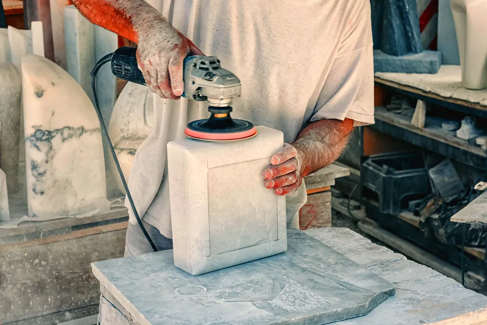 A stoneworker shaping a marble block with a hand tool.