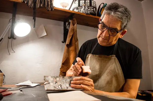 A maker at his bench under a work lamp, tools hung above.